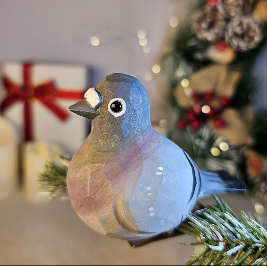 Hand-carved gray basswood pigeon clip-on ornament perched on a pine branch with blurred Christmas lights in the background.