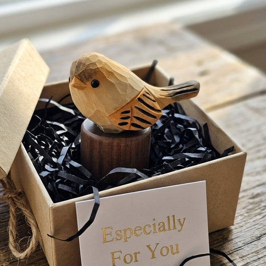 A small carved wooden bird figurine displayed inside an open kraft gift box with black shredded paper filler and a card that reads 'Especially For You'.