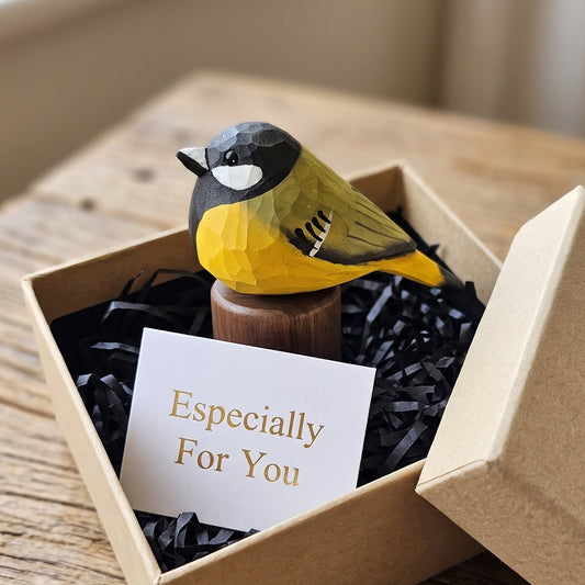 A small Great Tit figurine with a yellow and olive-green body, black head, and white eye, displayed inside a kraft gift box with black shredded paper and a card that reads 'Especially For You.'.