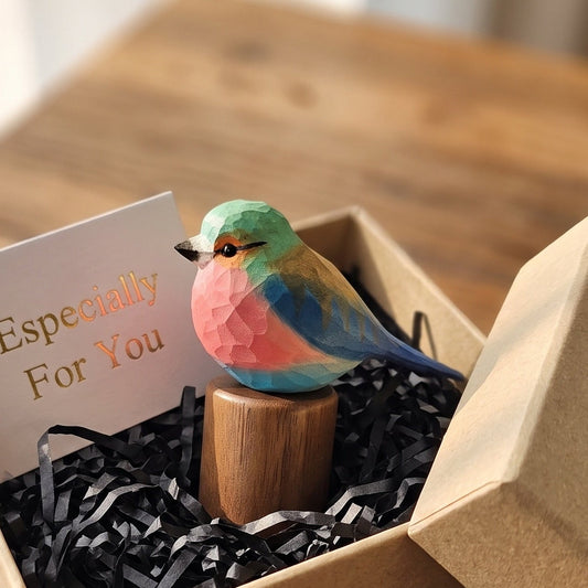 A small colorful Lilac-breasted roller figurine perched on a wooden stand inside a kraft gift box with black paper filler and a card that reads 'Especially For You,' set on a wooden table.