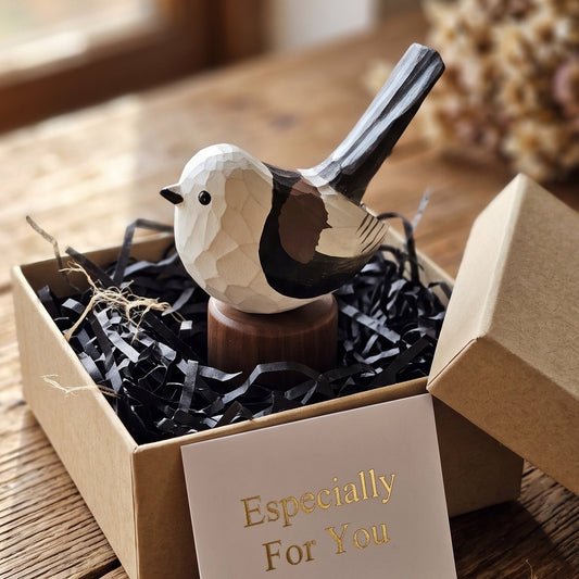 A carved wooden Long-tailed tit figurine with a white, black, and brown geometric pattern sits in a small kraft gift box filled with black shredded paper. A card in front reads 'Especially For You'.