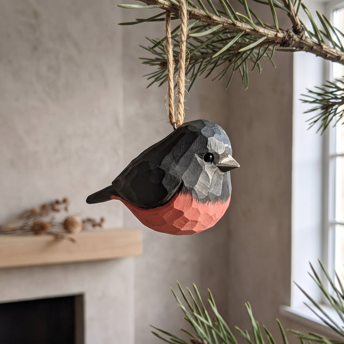 Hand-carved basswood pink robin hanging Christmas tree ornament on a pine branch.