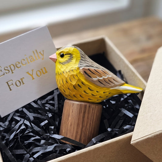 A small yellow Yellowhammer figurine perched on a wooden block, presented inside a kraft gift box with black shredded paper and a card that reads 'Especially For You'.