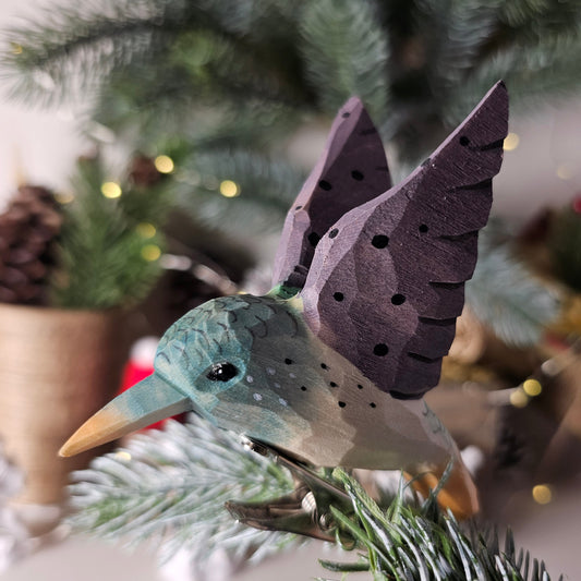 Hand-carved wooden purple hummingbird clip-on ornament perched on a pine branch.