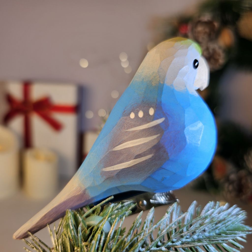 A hand-carved wooden blue lovebird clip-on ornament shown in profile, featuring a bright turquoise-blue body, subtle white-striped wing accents, a dark eye and beak, and a silver clip attached underneath.
