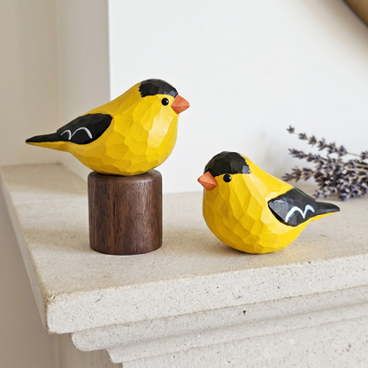 Two yellow American Goldfinch figurines on a stone surface with a blurred background