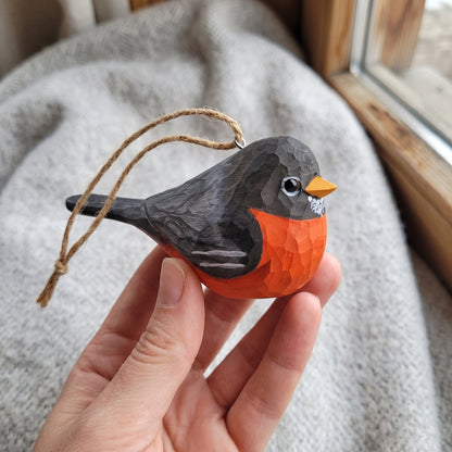 Person holding a hand-carved wooden American Robin bird ornament with a twine hanging loop.
