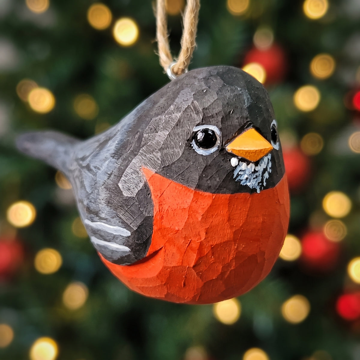 Hand-carved wooden American Robin ornament hanging in front of blurred Christmas tree lights.