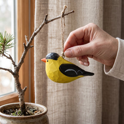 Hand placing a hand-carved wooden American Goldfinch ornament onto a potted branch indoors