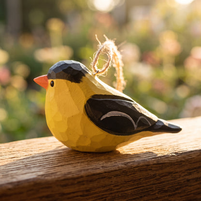 Hand-carved wooden American Goldfinch ornament resting on a wooden ledge outdoors