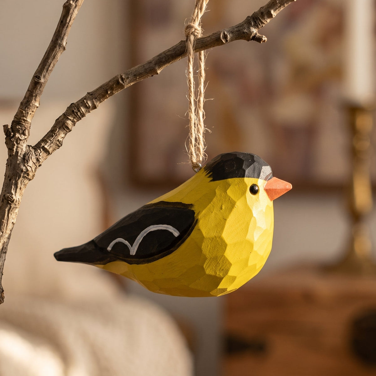 Hand-carved wooden American Goldfinch hanging ornament on a rustic branch