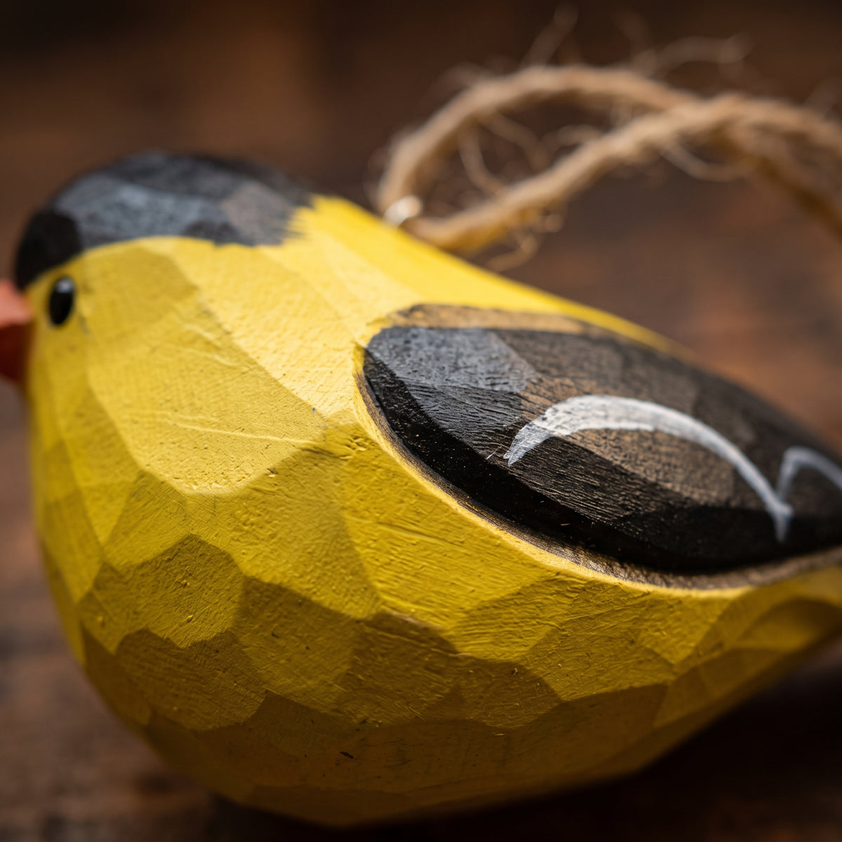 Macro close-up showing hand-carved wood texture and yellow paint on an American Goldfinch ornament