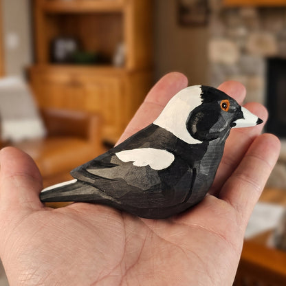 Handheld view of a hand-carved wooden Australian Magpie figurine with black and white plumage, detailed wing markings, and an orange eye resting in an open palm