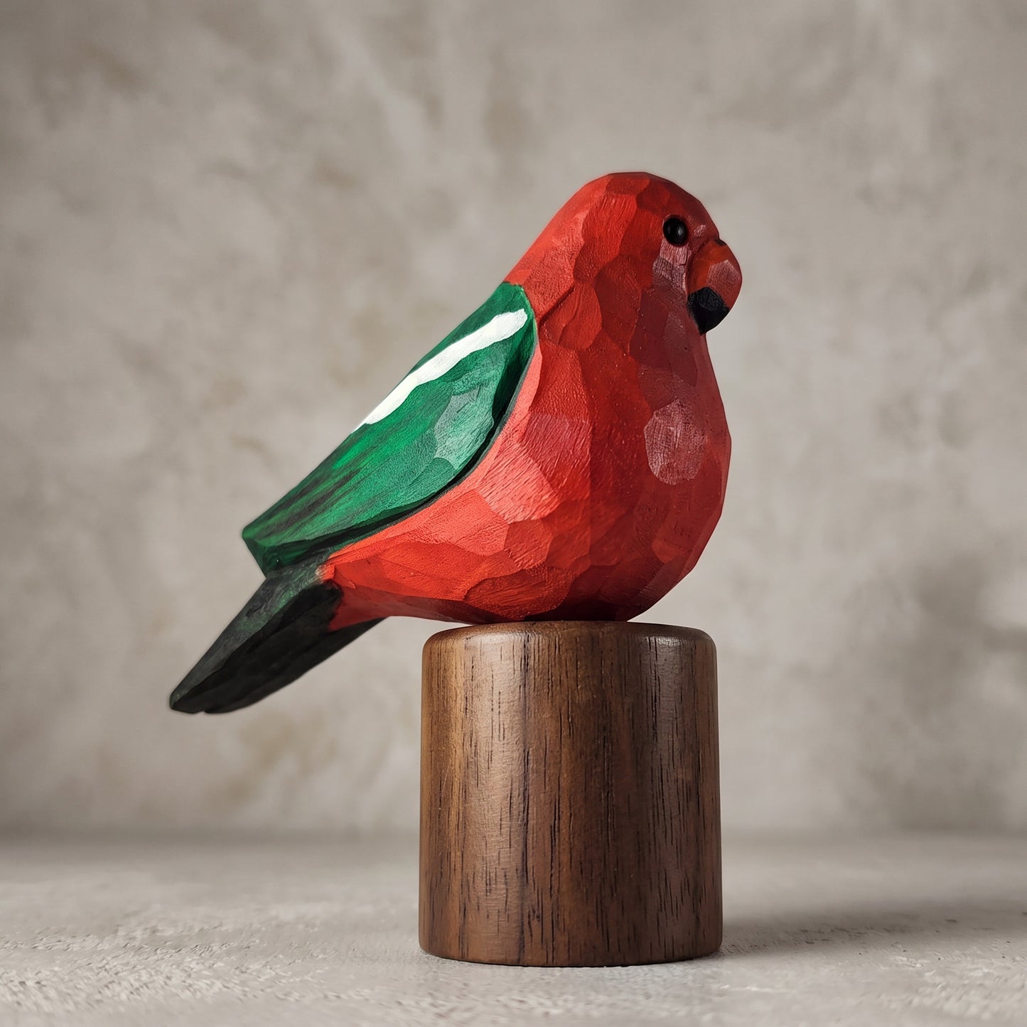 Side profile of a hand-carved wooden Australian King Parrot figurine with a vibrant red body, green wing, and black tail, mounted on a solid Black Walnut cylinder base.