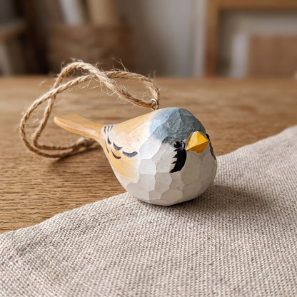Hand-carved wooden Bearded Tit bird ornament resting on a textured linen mat with a twine hanging loop.