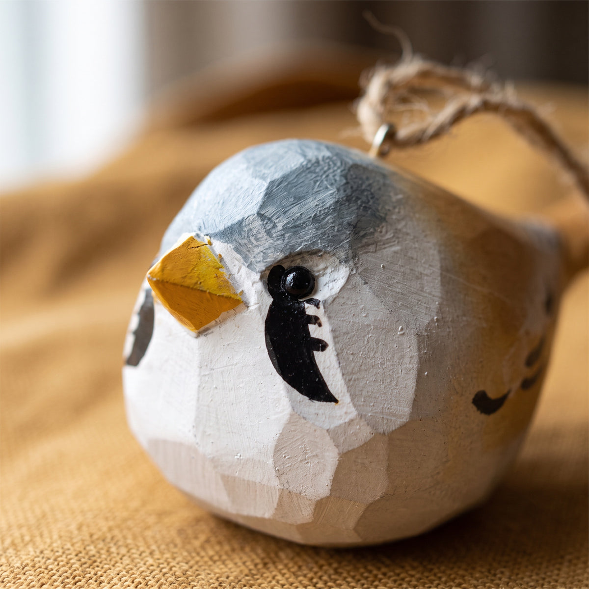 Close-up of a hand-carved wooden Bearded Tit bird ornament resting on warm yellow fabric.