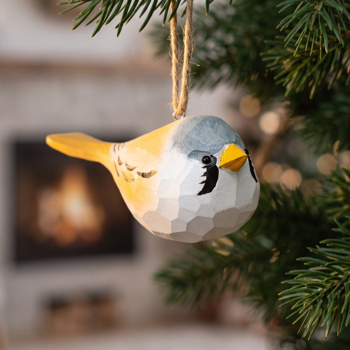 Hand-carved wooden Bearded Tit ornament hanging from a pine branch on a Christmas tree.