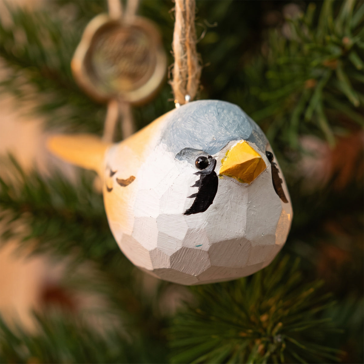 Front-facing close-up of a hand-carved wooden Bearded Tit bird ornament hanging from a pine tree branch.