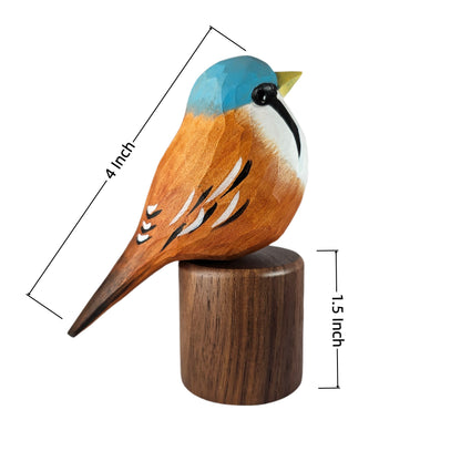 A carved wooden Bearded reedling figurine with a blue cap, orange-brown body, white chest, and yellow beak, mounted on a cylindrical wooden base. Black dimension lines and text show 4 inch length and 1.