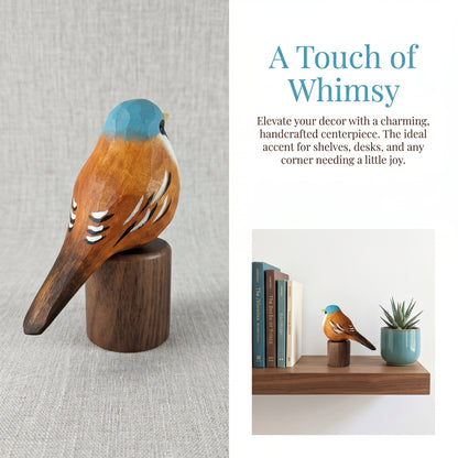 A handcrafted wooden Bearded reedling centerpiece with a blue-topped head and white feather details, displayed on a cylindrical wooden base. The left side shows the sculpture on a textured light gray fabric background, while the right side features a text overlay reading 'A Touch of Whimsy' and a smaller lifestyle inset showing the bird decor styled on a shelf next to books and a small plant.