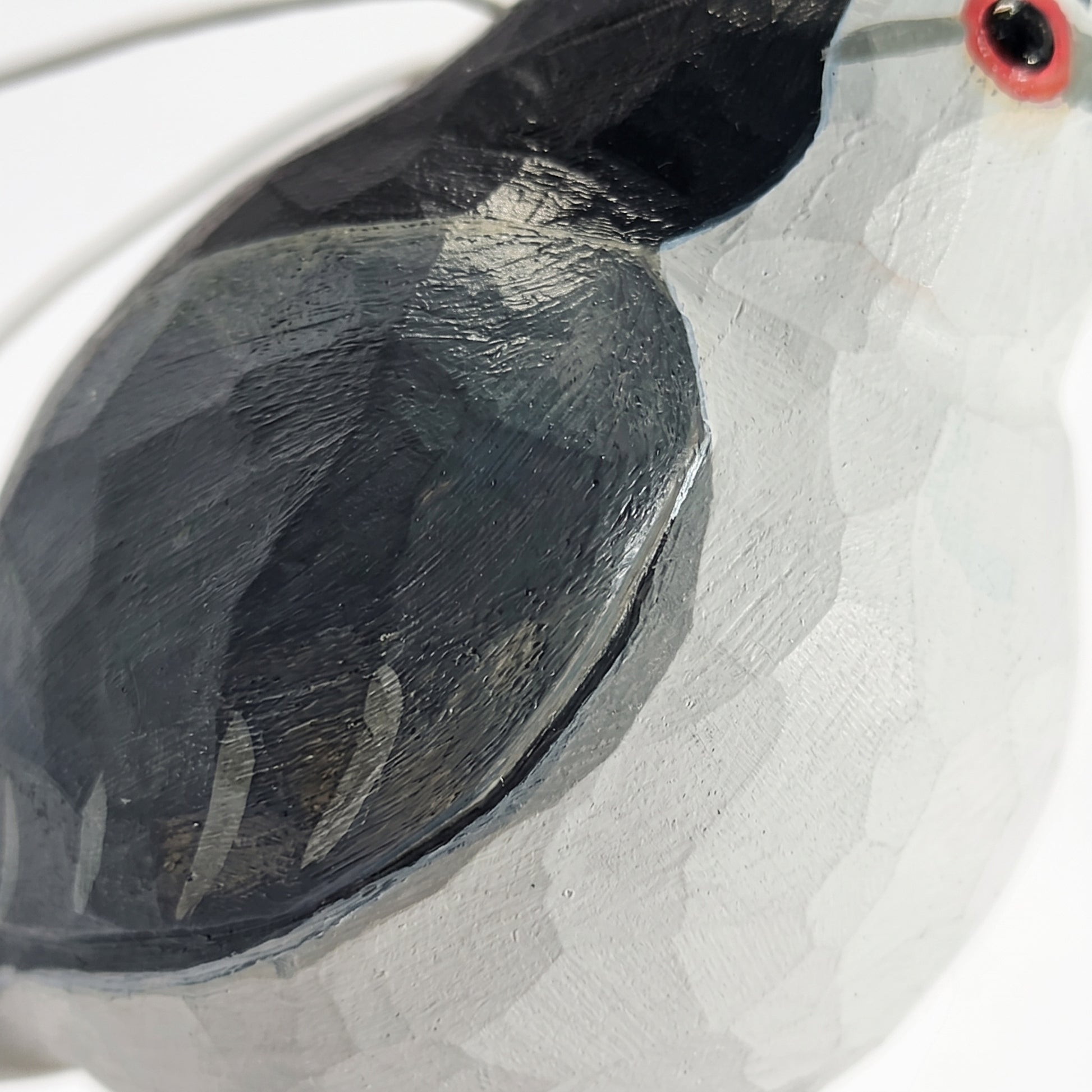 Close-up of a hand-painted wooden Black-crowned Night Heron sculpture, showing a textured white body, a dark charcoal-black wing, and a small red and black eye detail on a plain white background.