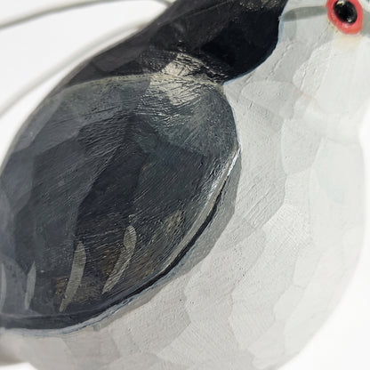 Close-up of a hand-painted wooden Black-crowned Night Heron sculpture, showing a textured white body, a dark charcoal-black wing, and a small red and black eye detail on a plain white background.
