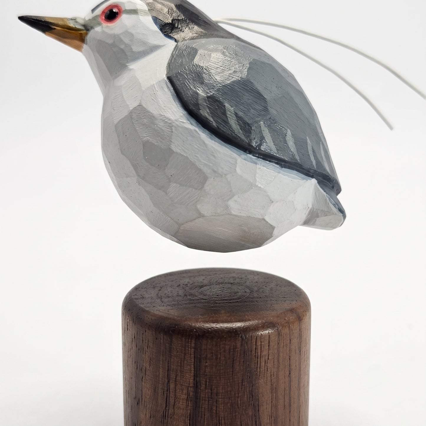 A geometric, faceted Black-crowned Night Heron sculpture mounted on a dark wooden cylinder base, photographed against a clean white background.