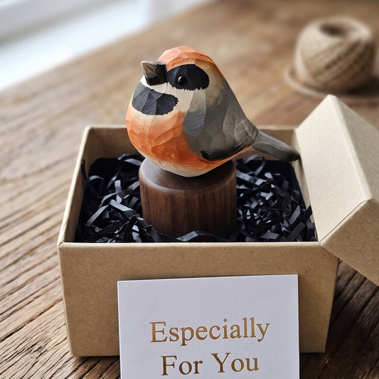 A small wooden Black-throated bushtit figurine with orange, gray, and black painted details sits in a brown kraft gift box filled with black shredded paper. A white card in front reads 'Especially For You.