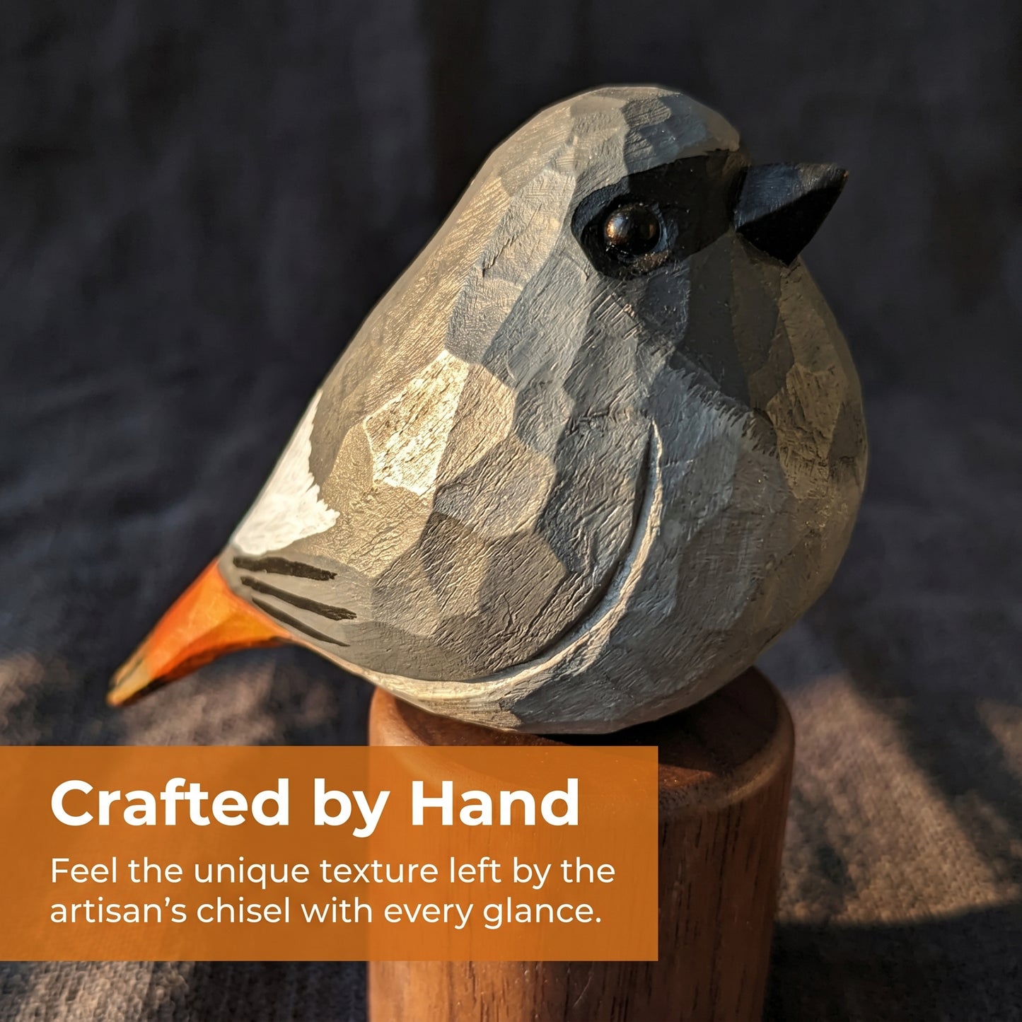 A hand-carved wooden Black redstart sculpture with geometric facets, shown perched on a wooden stand against a dark textured background. An orange text banner at the bottom reads, 'Crafted by Hand.