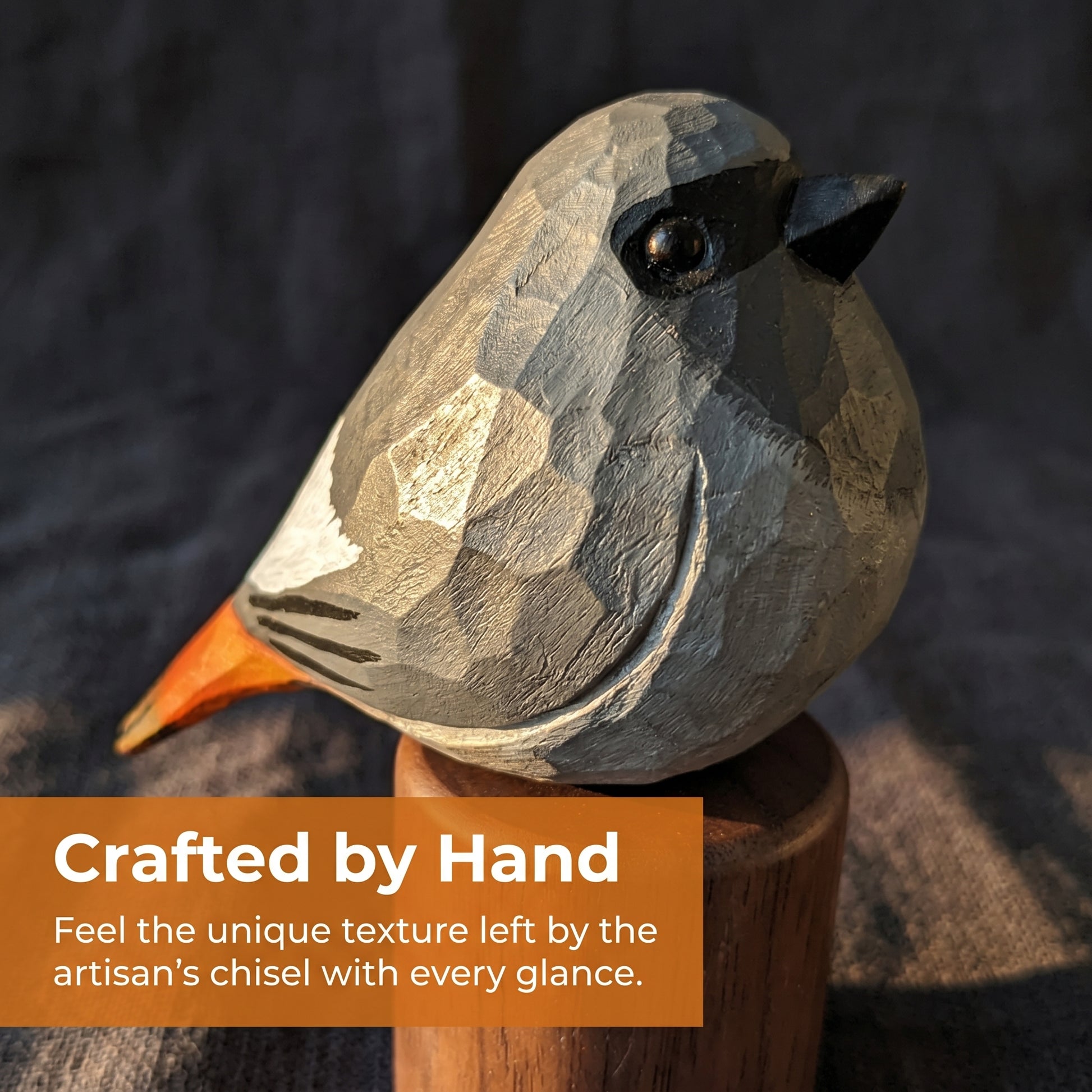 A hand-carved wooden Black redstart sculpture with geometric facets, shown perched on a wooden stand against a dark textured background. An orange text banner at the bottom reads, 'Crafted by Hand.