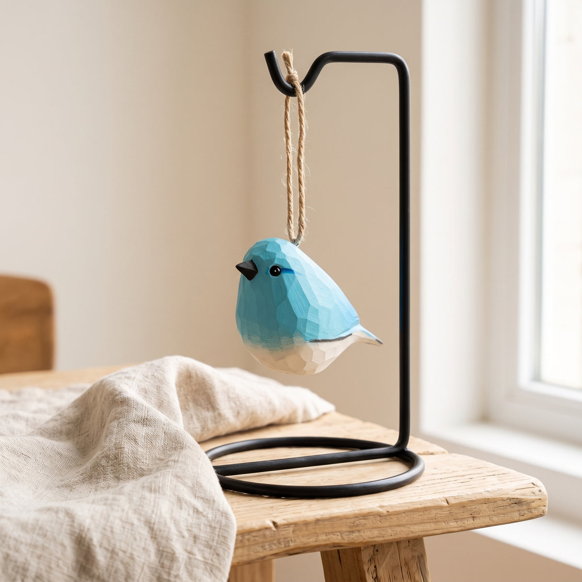 Hand-carved wooden bluebird ornament displayed on a black metal stand on a wooden tabletop