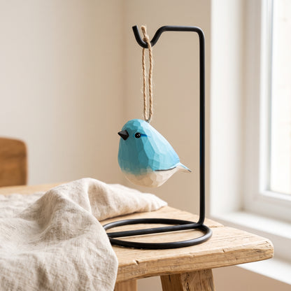 Hand-carved wooden bluebird ornament displayed on a black metal stand on a wooden tabletop