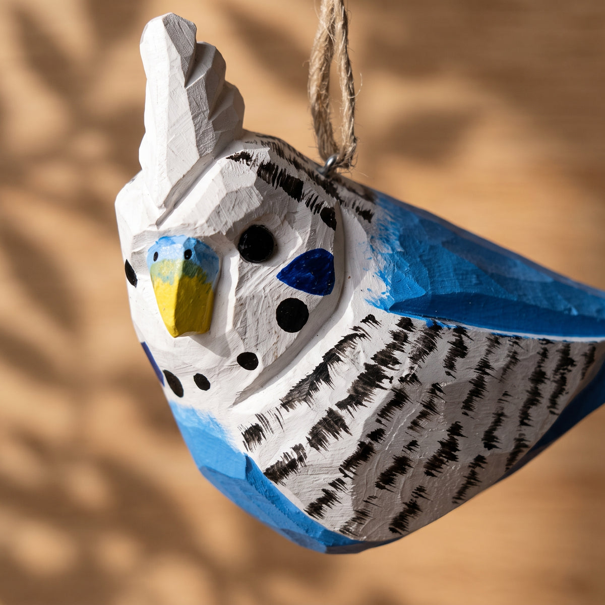 Close-up of hand-carved blue and white wooden budgie ornament showing detailed painted feathers and hanging twine