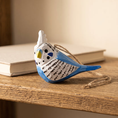 Hand-carved blue and white wooden budgie ornament resting on a wooden table next to an open book
