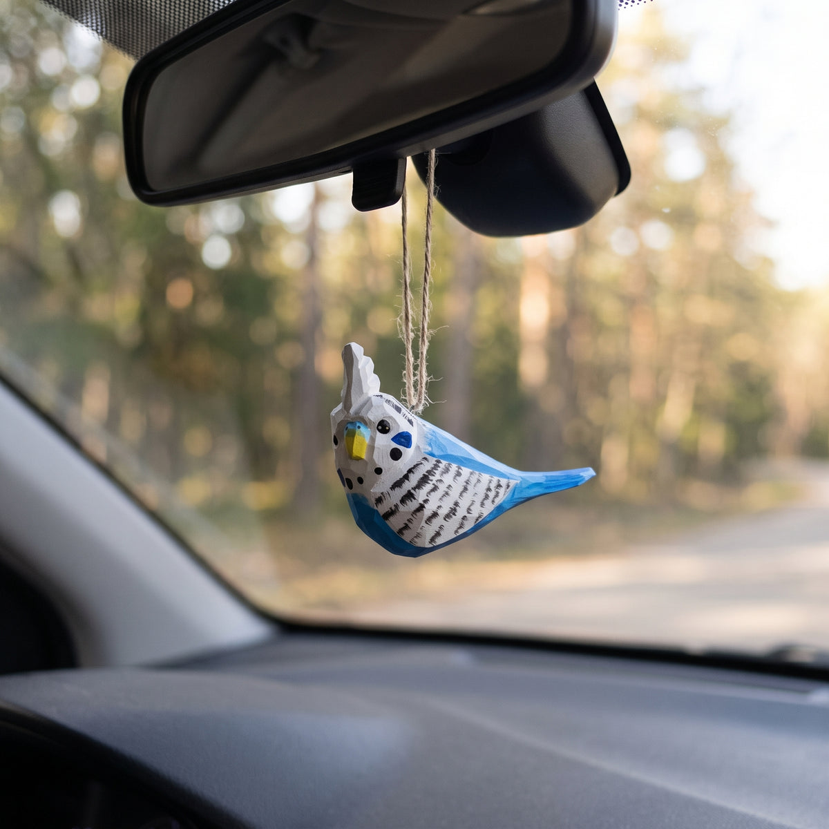 Hand-carved blue and white wooden budgie ornament hanging from a car rearview mirror