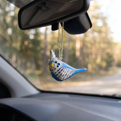 Hand-carved blue and white wooden budgie ornament hanging from a car rearview mirror