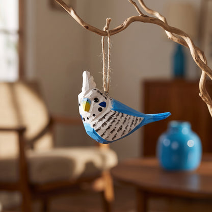 Hand-carved blue and white wooden budgie ornament hanging from a natural tree branch indoors