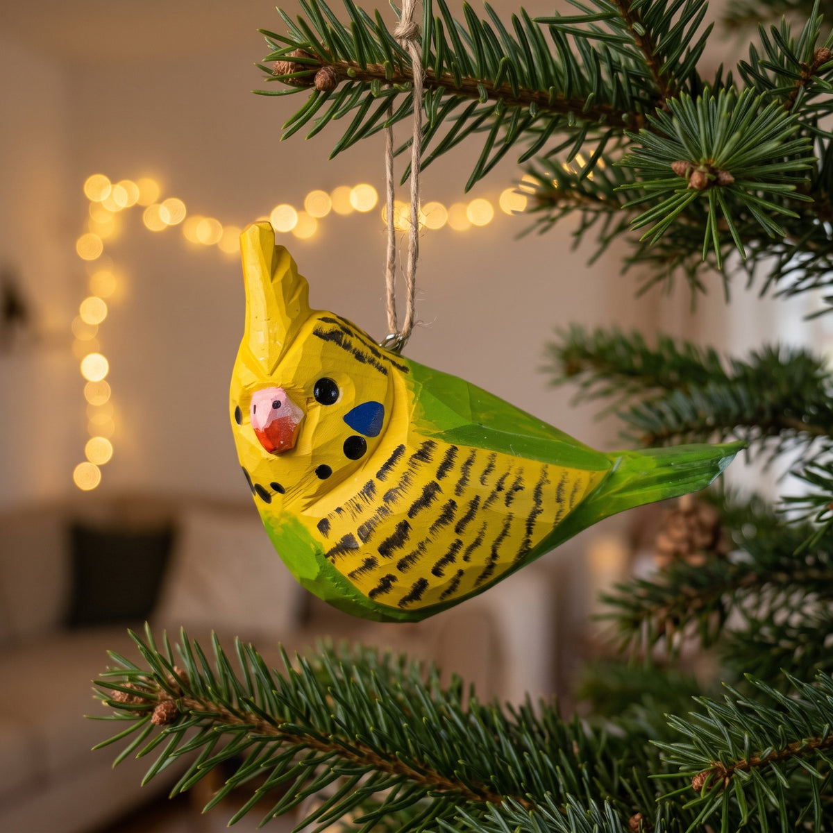 Hand-carved yellow and green wooden cockatiel budgie ornament hanging on a pine tree branch