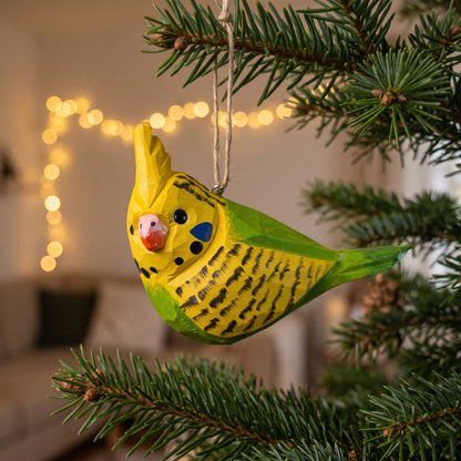 Hand-carved yellow and green wooden cockatiel budgie ornament hanging on a pine tree branch