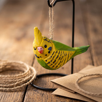 Yellow and green hand-carved wooden cockatiel budgie ornament hanging on a metal stand over a wooden table