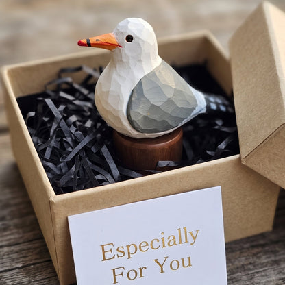 A geometric, low-poly style wooden California gull figurine with a white head, gray wing, and orange beak, displayed inside a brown kraft gift box filled with black paper shred. A white card in front reads 'Especially For You'.