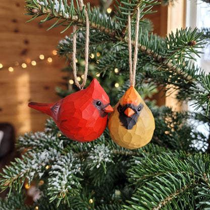 Two faceted bird Christmas ornaments hanging on a pine tree branch. One ornament is bright red and the other is mustard yellow, both with black and orange facial details, suspended by twine in a decorated Christmas tree setting.