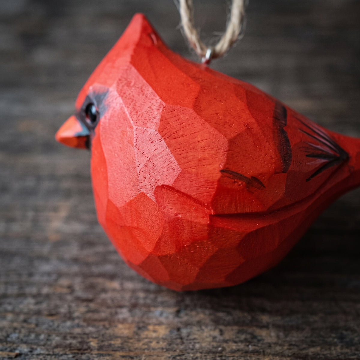 A red carved wooden cardinal bird ornament with a hanging twine loop, photographed close up on a rustic dark wood surface.