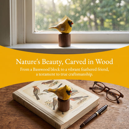 A carved wooden Yellow Cardinal figurine in bright yellow and brown stands on a wooden surface in a styled interior scene, with an open bird-print book, eyeglasses, and a pen nearby. A large yellow banner across the center reads, 'Nature's Beauty, Carved in Wood' and smaller text follows.