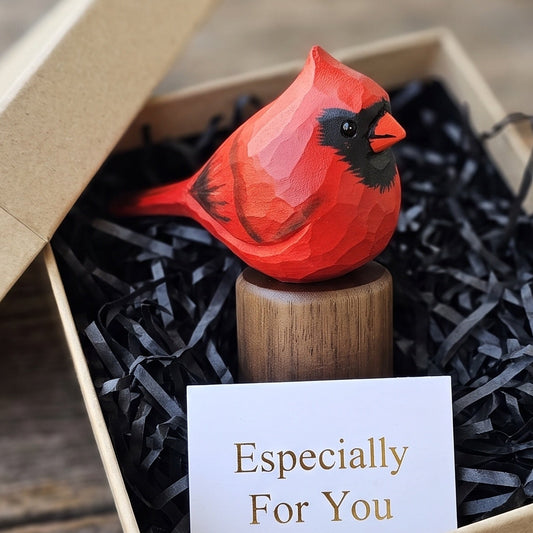 A red cardinal figurine displayed in a kraft gift box with black shredded paper filler and a small card that reads 'Especially For You,' set on a rustic wooden surface.