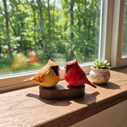 Two handcrafted wooden cardinal bird sculptures on a dark wooden base, displayed on a wooden windowsill with a small potted succulent in the background.