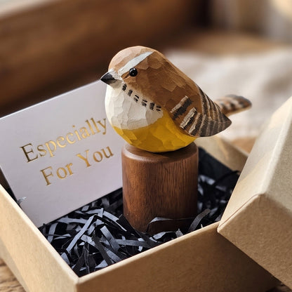 A handcrafted wooden Carolina Wren figurine with a yellow belly and brown striped wings, displayed on a wooden stand inside a kraft gift box with a card that reads 'Especially For You'.