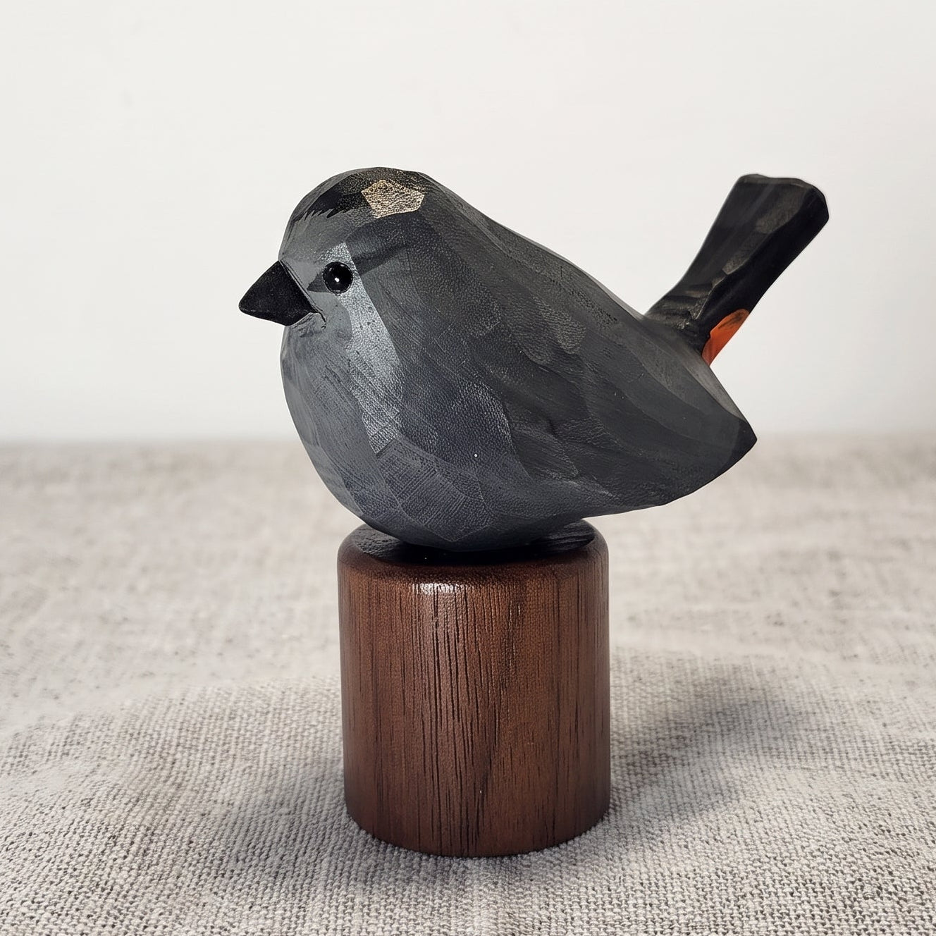 A hand-carved Gray Catbird figurine in slate-gray with a black cap, perched on a cylindrical Black Walnut base against a neutral background.
