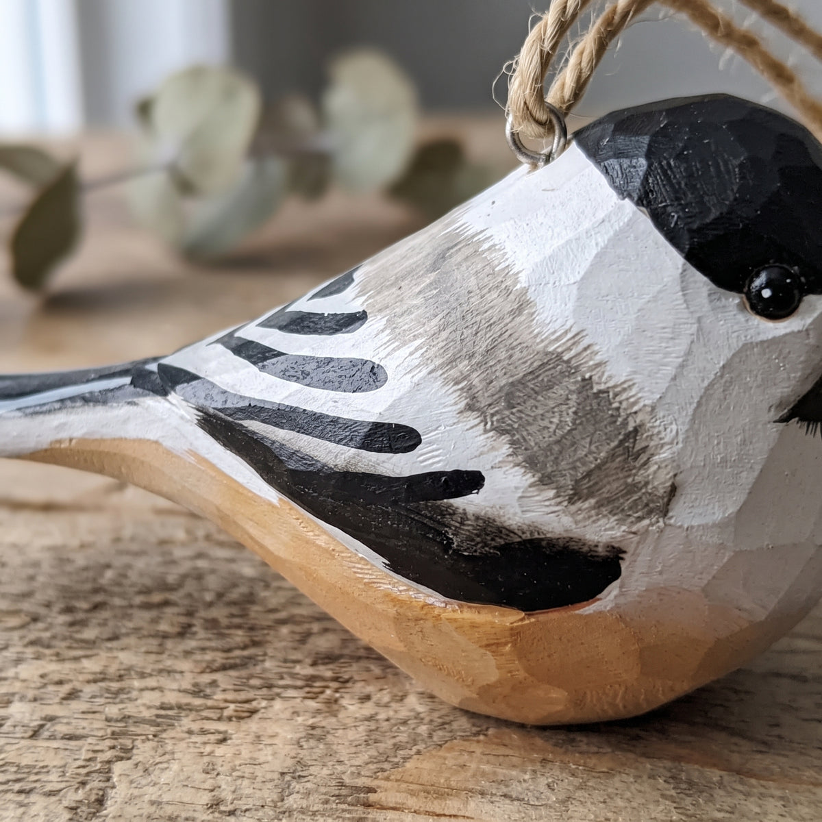 Close-up shot showing the hand-carved wood grain and hand-painted details of a Black-capped Chickadee hanging ornament with jute twine.