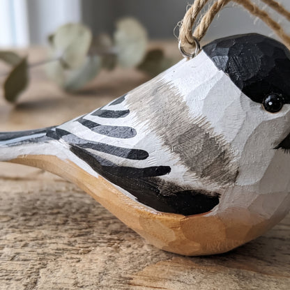 Close-up shot showing the hand-carved wood grain and hand-painted details of a Black-capped Chickadee hanging ornament with jute twine.